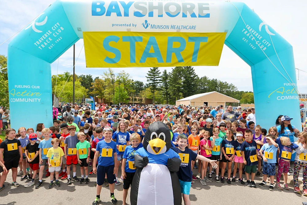 Kids gathered at a 5K start line under a blue inflatable arch with START banner and sponsor branding