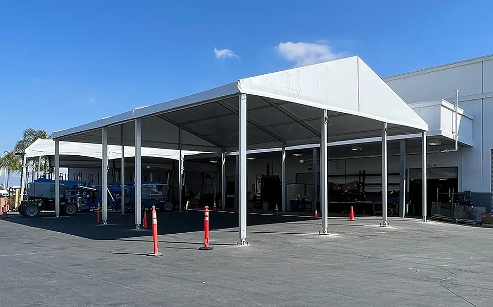 Industrial gable frame tent beside a building, providing covered space for operations and storage.