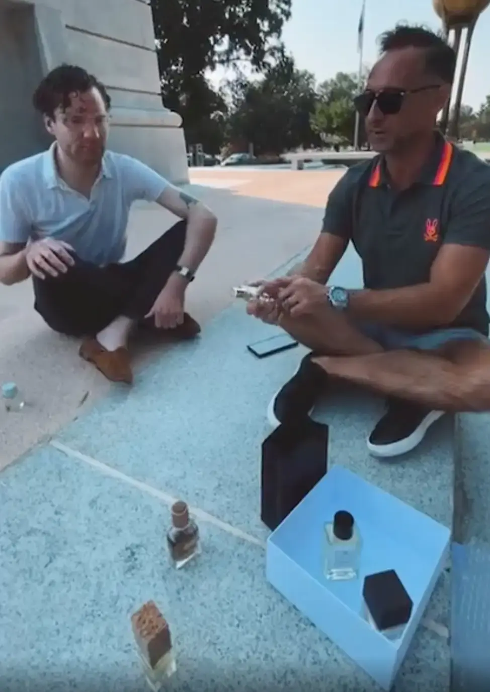 Two fragrance experts discussing signature scent recommendations outdoors with niche perfume bottles displayed in front of them.