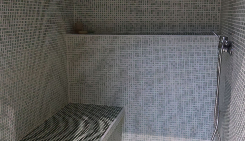 Intérieur d'un hammam avec banquettes en mosaïque bleue et grise, atmosphère de vapeur douce et éclairage tamisé