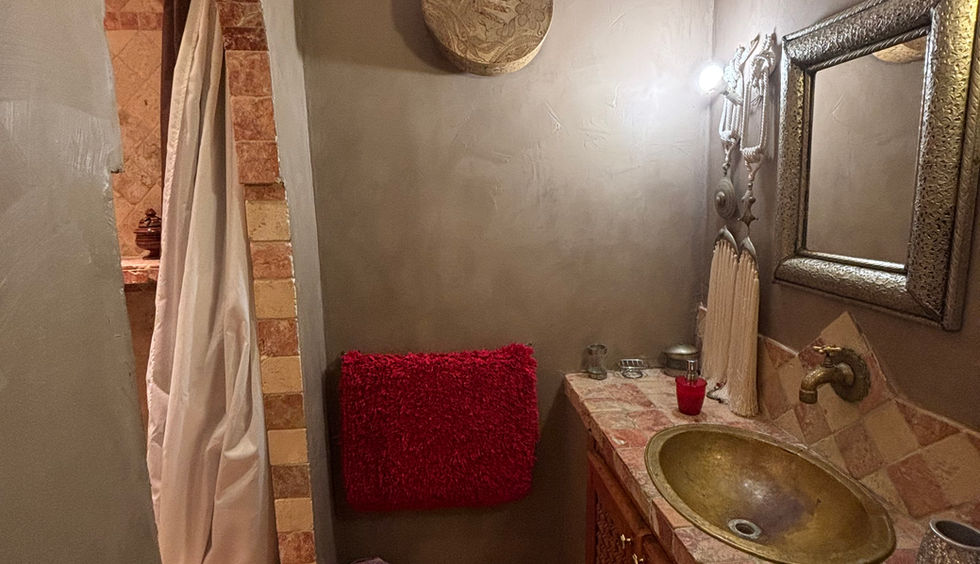 Salle de bain de spa avec vasque en laiton dorée, meubles en bois sculpté, murs à l'enduit naturel et décoration ethnique sous une lumière tamisée