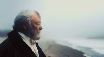 Plan moyen de profil sur un Victor Hugo barbu et contrarié, qui fixe l'horizon sur une plage de Guernesey. On devine qu'il a les yeux tournés vers la France, qui lui manque.
