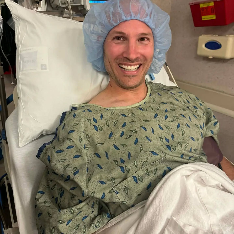 A man is lying down in a hospital bed wearing a hospital gown and surgical cap awaiting surgery.