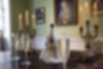 Table in Dr Johnson's withdrawing room with a bottle of prosecco, three filled glassed and two candelabras on the table, with a painting on the wall behind
