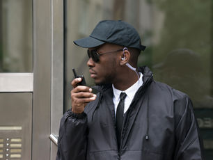 Security guard reporting a checkpoint by radio outside a building — proof of patrol app