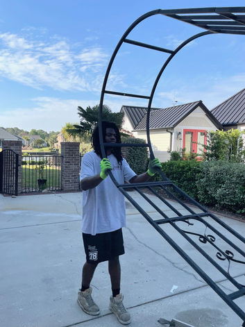 A Yarborough’s Moving Service team member carries a large wrought iron garden arbor across a driveway in a Myrtle Beach neighborhood. Their professional handling ensures safe transport of oversized and delicate outdoor furniture.
