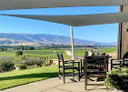 Outdoor furniture setting under shade sail looking over garden, vines to the mountains beyond.  Bannock Brae Central Otago NZ