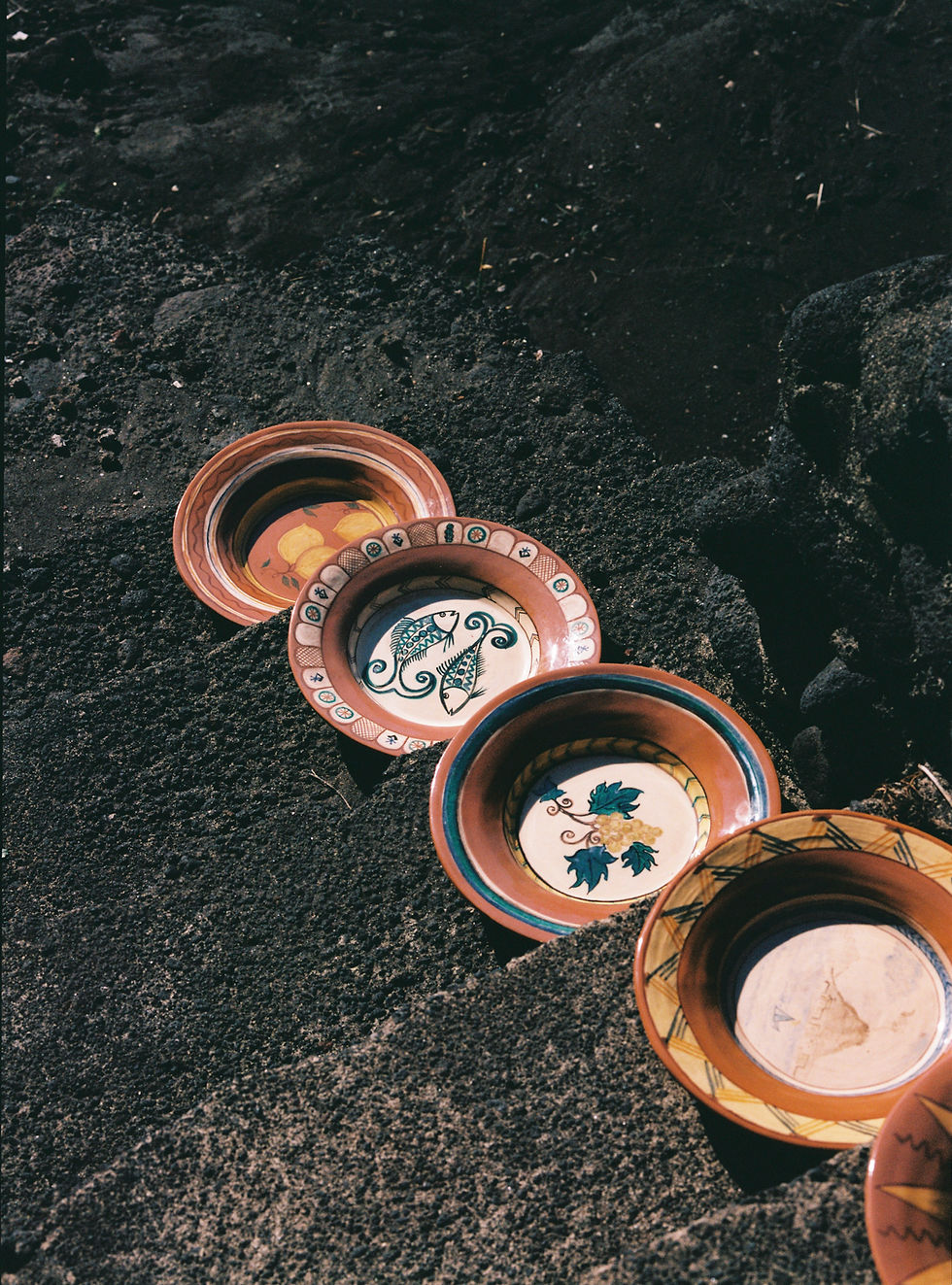 Four decorative plates with fish and leaf designs on dark stone steps. Warm browns and intricate patterns create a rustic, earthy feel.