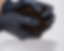 A close-up of two gloved hands (nitrile gloves, black or blue) squeezing a handful of dark brown substrate — ideally coco coir or sawdust mix — over a clean white surface or bowl.