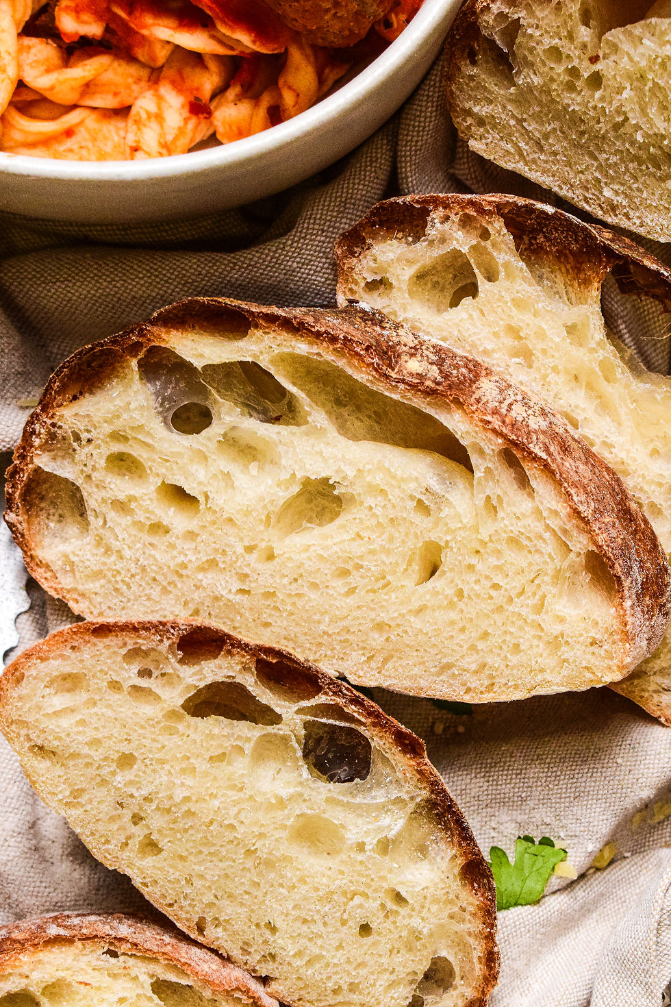 Rustic homemade ciabatta bread with pasta and meatballs in the background