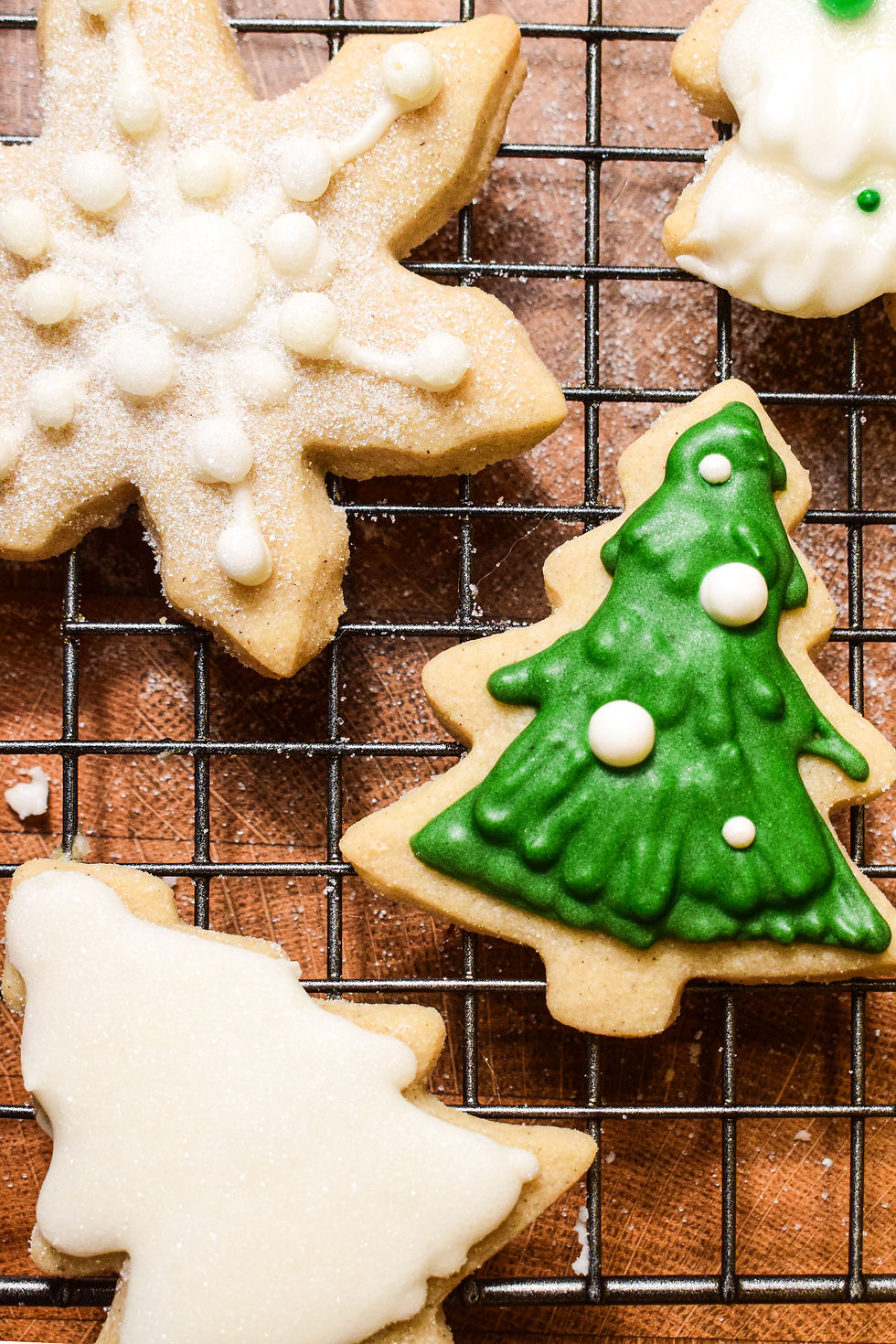 Festive cookies shaped like a snowflake and Christmas trees on a metal cooling rack. Green and white icing, sprinkled with sugar.