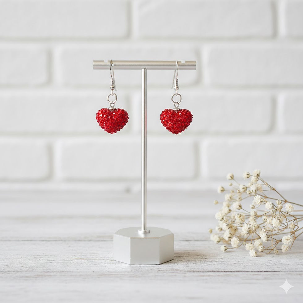 Two sparkling red heat earrings hanging on a T shaped holder with white brick and baby's breath on the side in background.