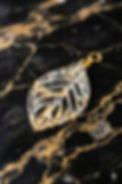 Clear resin leaf earring with gold flakes on black and gold marble. Botanical skeleton jewelry, nature-inspired design.