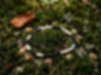 An agate, howlite, dyed shell beaded bracelet rests on a lush bed of green moss and small pebbles in a forest setting.