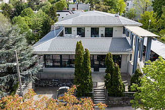 Modern multi-story building with a grey roof and green trees