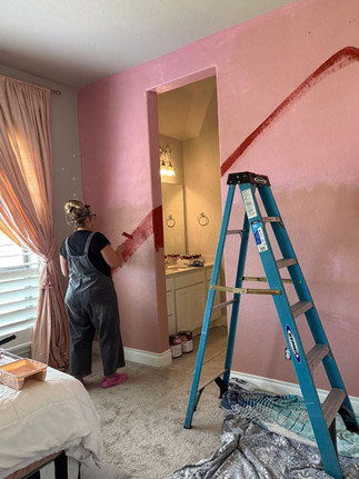 a woman using a paint roller to create the red rock design in various shades of red on the diy desert wall mural