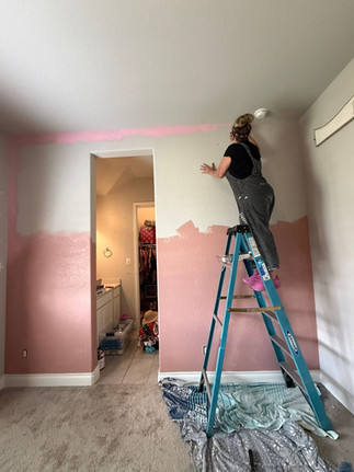woman starting to painting the top half of a bedroom wall as the first step in creating a diy desert wall mural