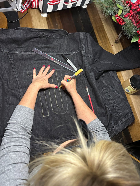woman outlining letters on back of men's custom painted denim jacket