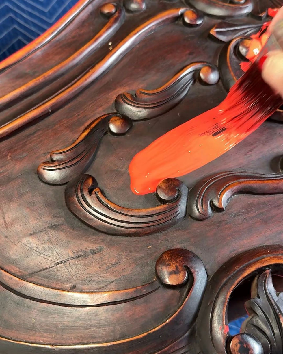how to paint carved wood furniture - first stroke of red paint on heavy carved dark wood headboard