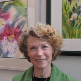 Artist Robbie Laird posing for her picture standing in an art gallery in front of a few framed paintings of hers 
