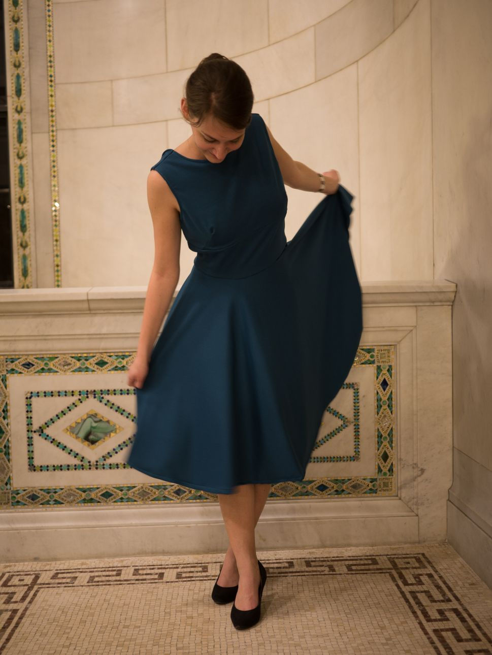 Une femme portant une robe col bateau et jupe circulaire, bleue, pose sur un balcon en mosaique.