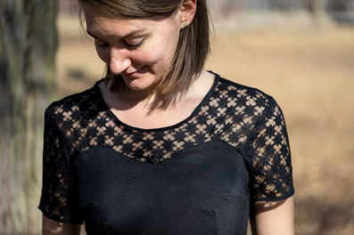 Une femme portant une petite robe noire, avec un haut en dentelle, est dehors, dans un jardin.