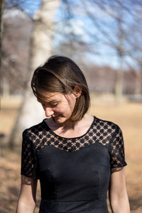 Une femme portant une petite robe noire, avec un haut en dentelle, est dehors, dans un jardin.