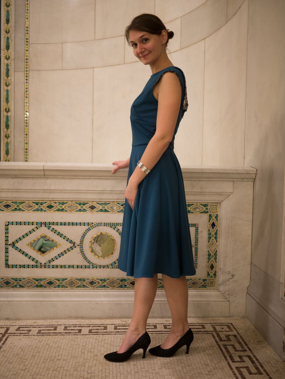 Une femme portant une robe col bateau et jupe circulaire, bleue, pose sur un balcon en mosaique.