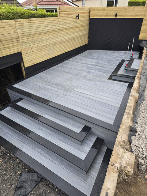 Grey composite decking with integrated steps and raised platform in a landscaped garden swansea