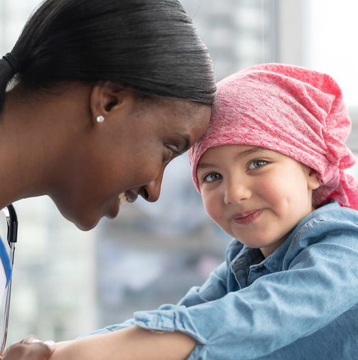 Female doctor smiling at young patient in pink head scarf.