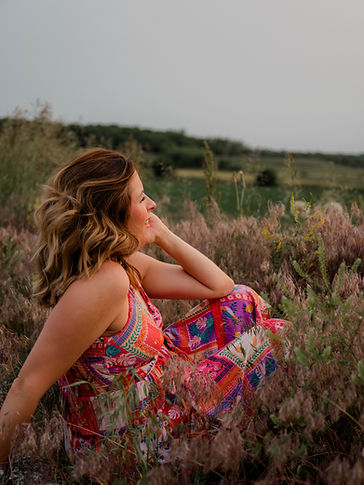 Emily sitting in field wearing a bright dress facing away from camera