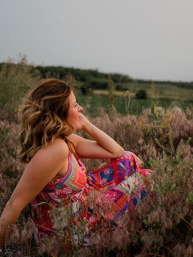 Emily sitting in field wearing a bright dress facing away from camera