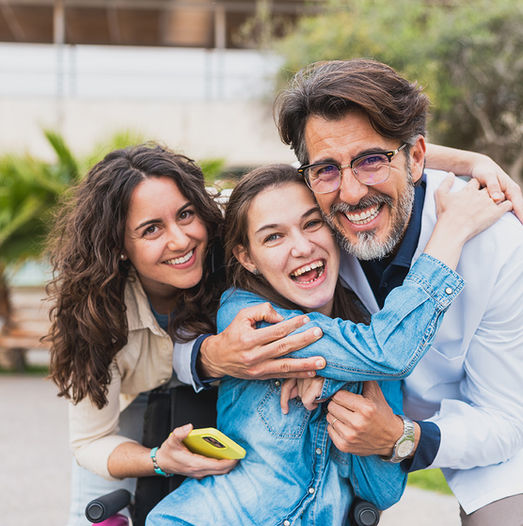 Male doctor smiling embraced by smiling mom and young female patient in wheel chair.