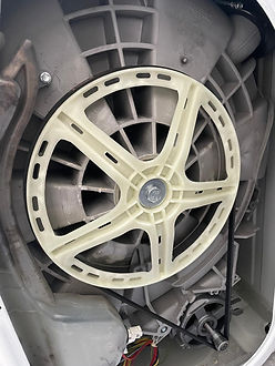 The rear panel of a white washing machine removed to show the internal motor mechanism