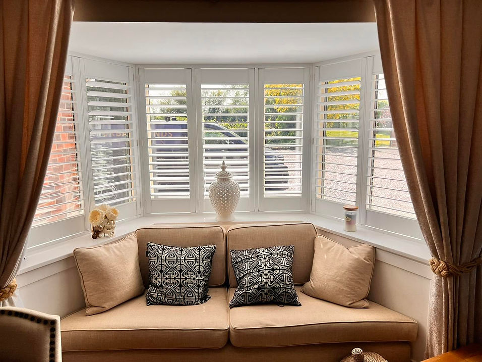 Shutters installed in bay window with warm curtains and chair