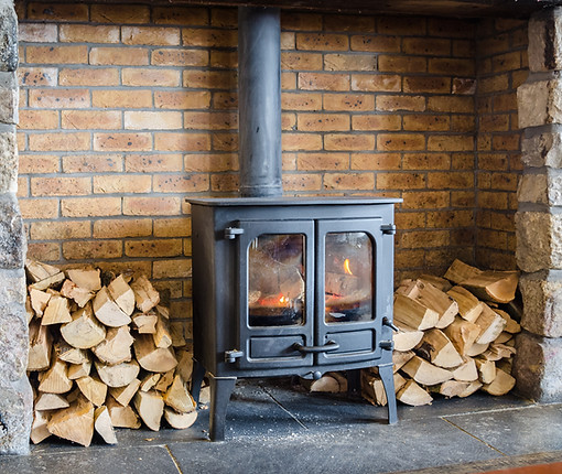 A cast iron fire in a stone fireplace with stacks of logs either side