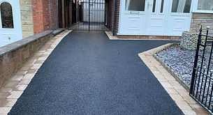 Freshly laid black tarmac driveway leading up to a residential property