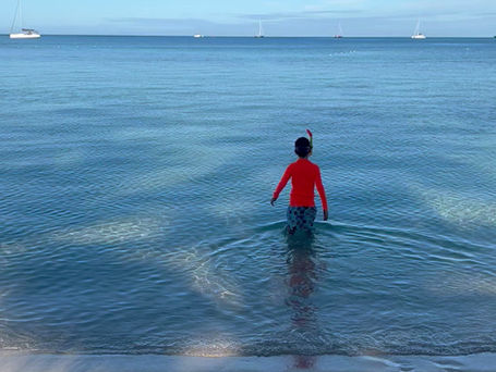 School-aged child walking in shallow tropical beach during family holiday 