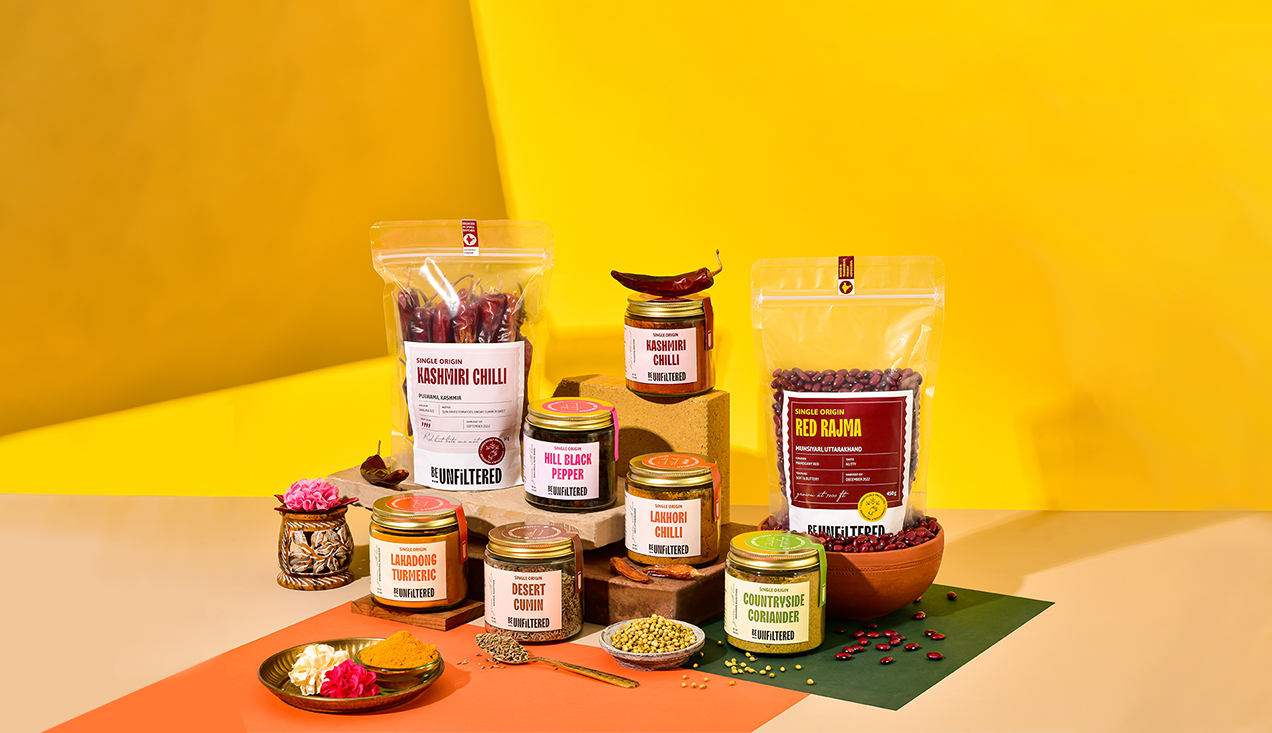 A collection shot from be unfiltered spices that includes Single Origin Kashmiri Chilli Whole, Single Origin Lakadong Turmeric Powder, Single Origin Black Peppercorns, Single Origin Cumin, Single Origin Kashmiri Chilli Powder, Single Origin Yellow Chilli Powder, Single Origin Coriander from Rajasthan and Munsiari Rajma. A whole range of spices and grocies that are organically grown and sourced from small farms in India.