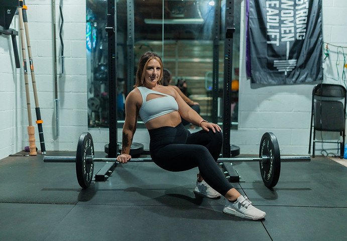 Laura Ash, Personal Trainer sits on a barbell looking at the camera.