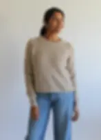 Smiling woman in beige sweater and blue jeans stands against a plain white background, exuding a relaxed and cheerful vibe. Located in North End Halifax.