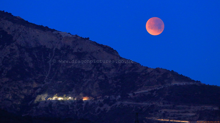 Bottom-aligned 16:9 crop of dawn light striking Minera de Órgiva, with a full lunar eclipse setting behind - authentic landscape photography with no digital enhancement, ideal for hotel decor.