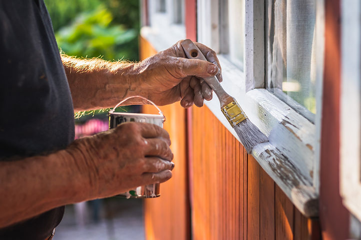 House improvement. Senior craftsperson is painting wooden window frame using paintbrush. O