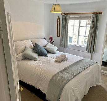A large bed with white and grey bedding with a window to the right of it