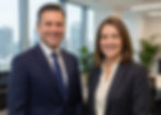 Two Board members smiling in an office with large windows and plants. Bright, professional atmosphere. No visible text.