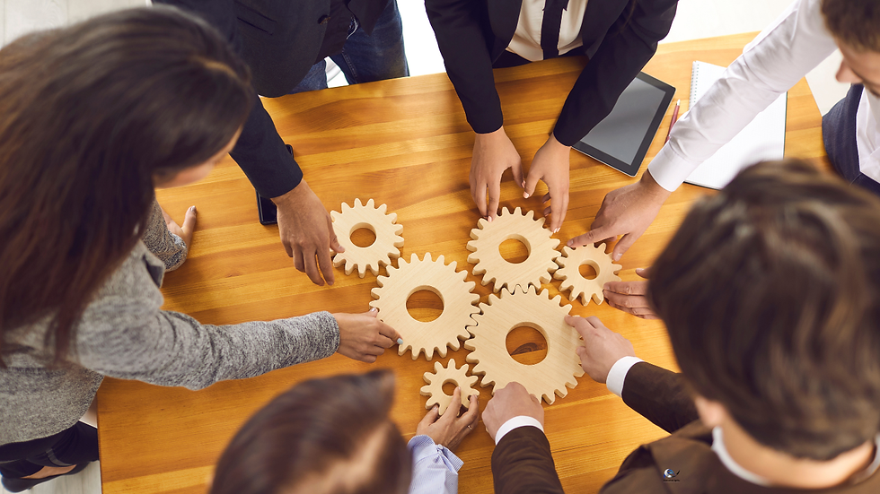 Team of coworkers arranging wooden gears on a conference table, symbolizing collaboration and teamwork in a bright office