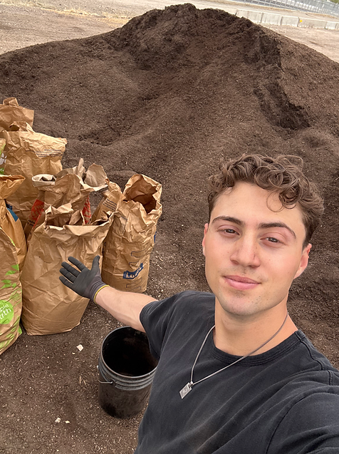 Melly's Recycling worker posing in front of paper compost bags and a large mound of organic compost soil.