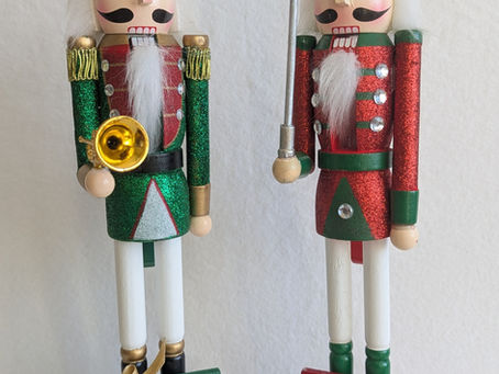 Two nutcrackers, holding various musical instruments and sharp objects. At their feet lie two plaques, one which says "The Nutcracker Two Ways", the other saying "2025".