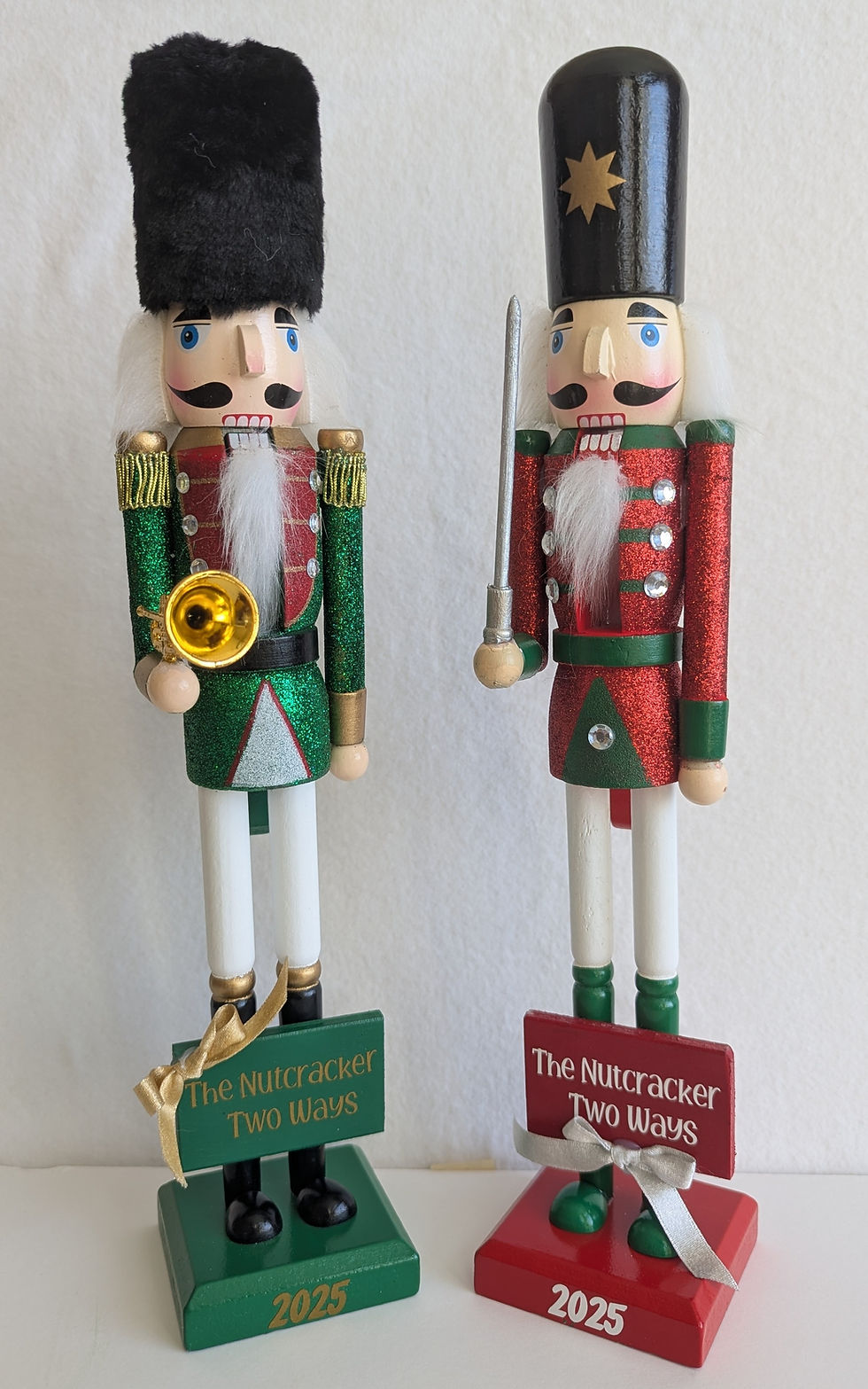 Two nutcrackers, holding various musical instruments and sharp objects. At their feet lie two plaques, one which says "The Nutcracker Two Ways", the other saying "2025".