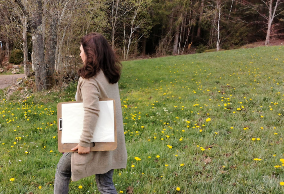 Woman walking across a grassy field carrying a drawing board under her arm.